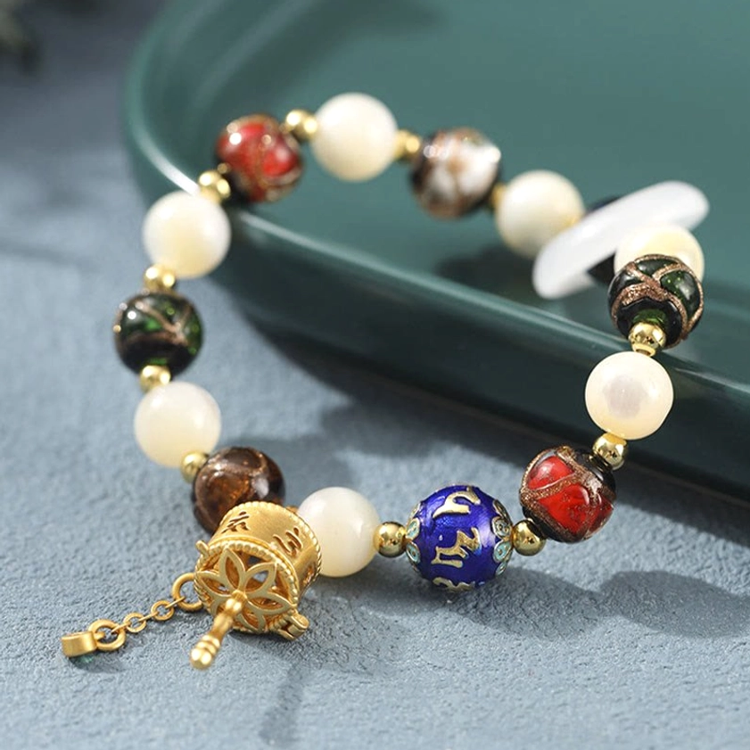 Tridacna stone and incense ash glass Buddhist bracelet with movable gilt prayer wheel pendant, side angle view