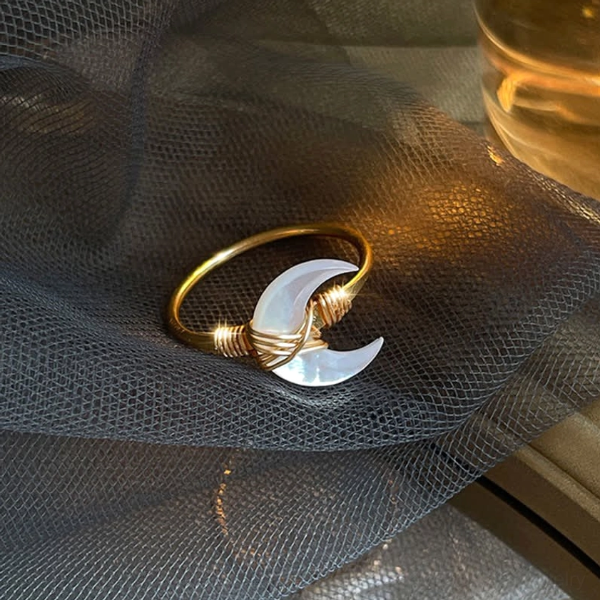 Single white tridacna stone moon blessing ring, flat lay product display on dark mesh surface