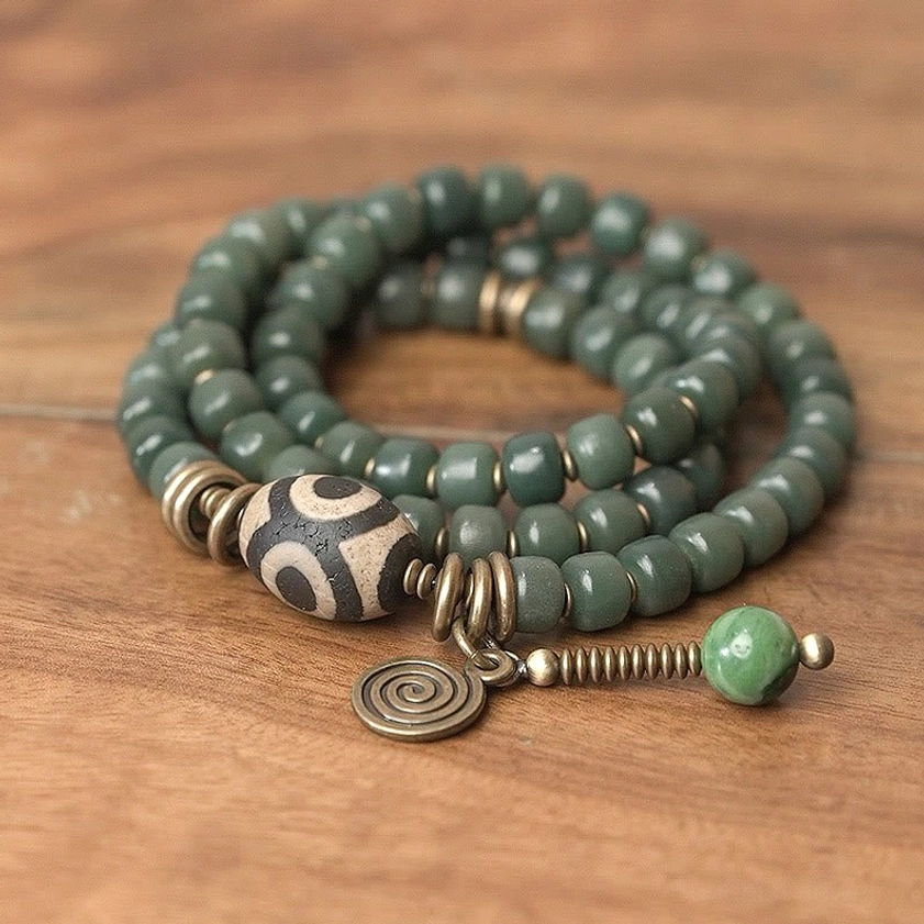 Multi-layer triple wrap dzi bead bracelet flat lay, displaying dark green stone beads and complete charm set