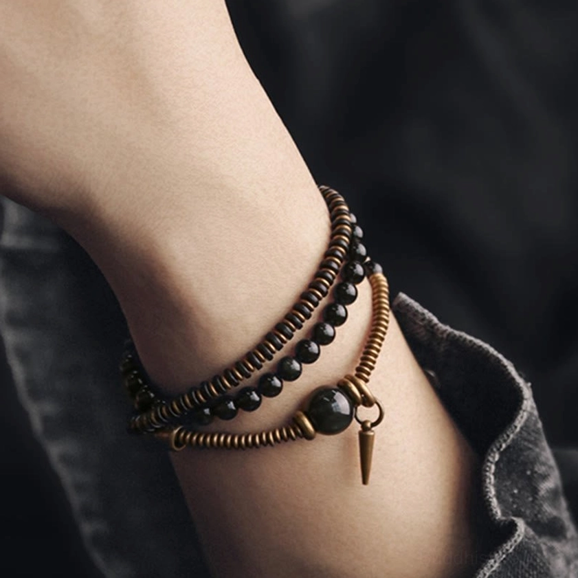 Triple wrap obsidian bracelet worn on wrist with denim cuff background, showing three-layer beaded design with cone pendant
