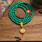 108-bead turquoise Buddhist prayer mala with dzi bead and pumpkin beads displayed on vintage textile, overhead view showing complete mala necklace