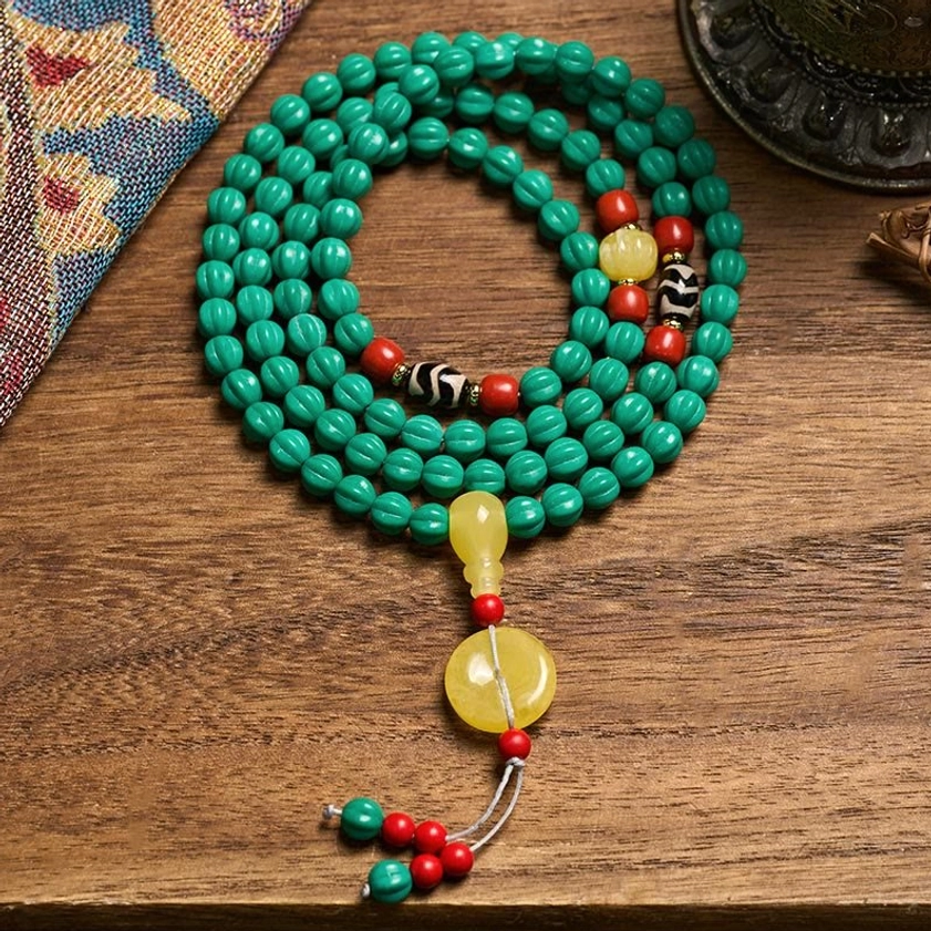 108-bead turquoise Buddhist prayer mala with dzi bead and pumpkin beads displayed on vintage textile, overhead view showing complete mala necklace
