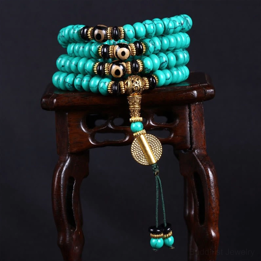Multi-strand turquoise mala with gold and green bead tassels on wooden stand