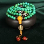108 bead turquoise Buddhist prayer mala necklace with three-eye dzi bead and amber guru bead on dark green velvet with ceramic bowl
