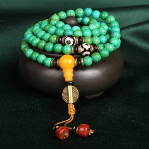 108 bead turquoise Buddhist prayer mala necklace with three-eye dzi bead and amber guru bead on dark green velvet with ceramic bowl