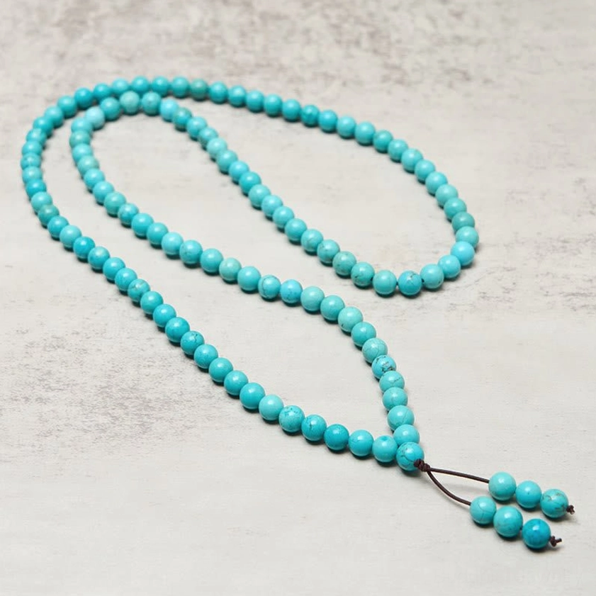 Turquoise mala beads laid out in long necklace format showing individual bead detail and leather tassel
