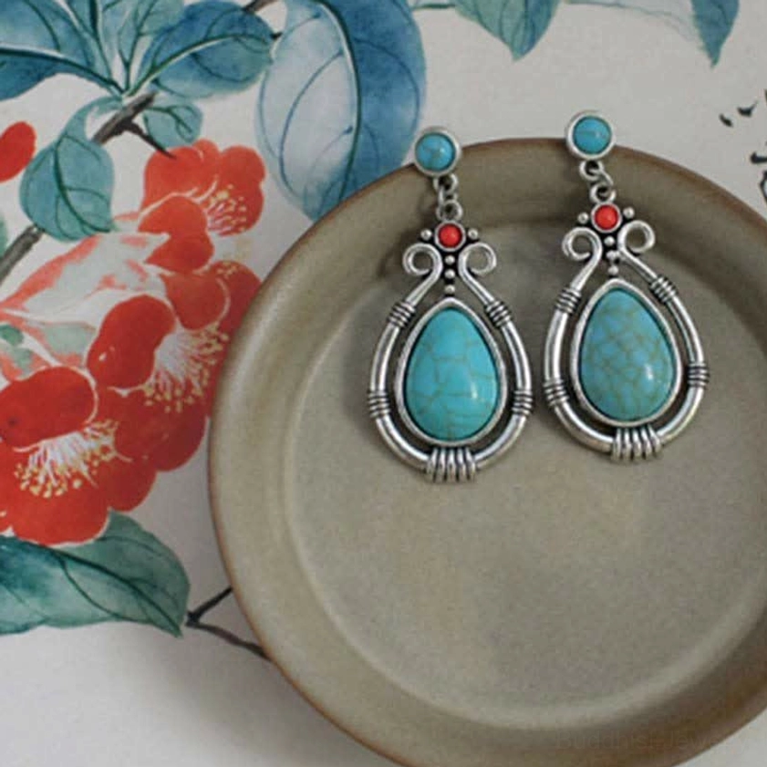 Turquoise dangle earrings placed on ceramic dish with traditional floral painting background