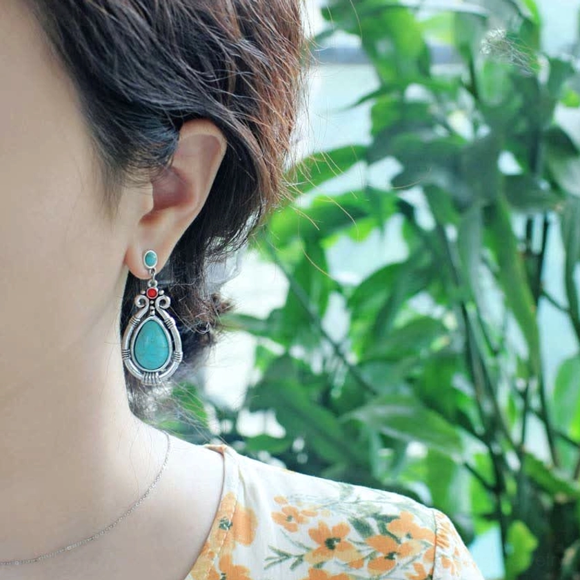 Woman wearing turquoise teardrop dangle earrings with green foliage showing daily wear style