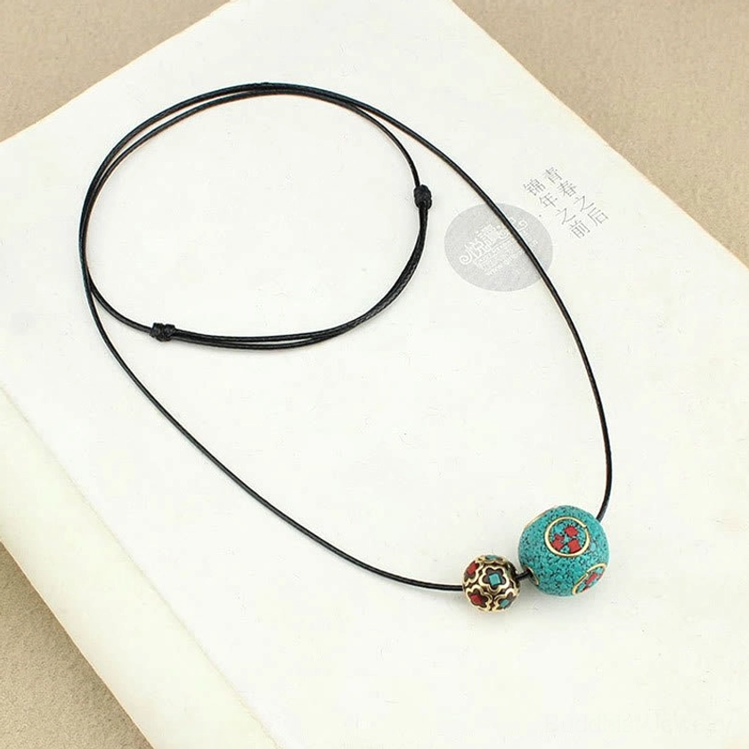 Turquoise double bead Buddhist necklace laid flat on open book pages showing adjustable ethnic cord