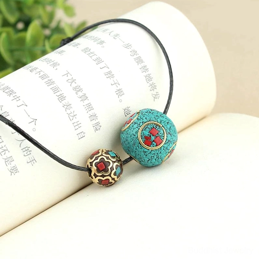 Artisan turquoise Buddhist protection necklace with gold-red patterned bead on open book with botanical background