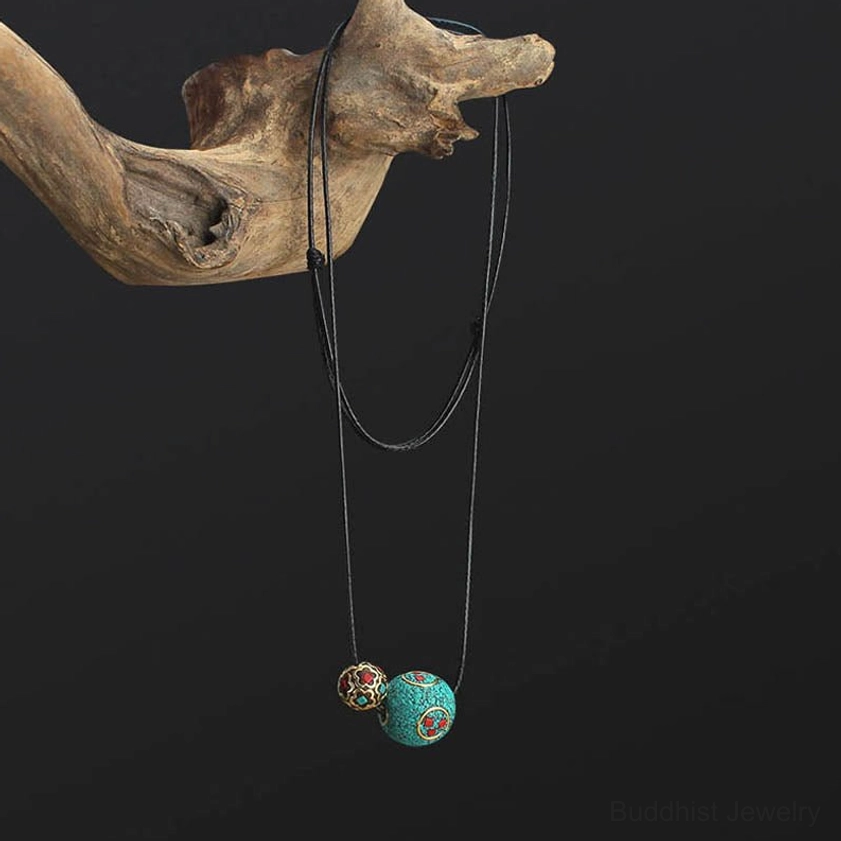 Handmade turquoise Buddhist protection necklace hanging from rustic wooden branch against black background, side profile view