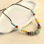 Handcrafted turquoise Buddhist beaded necklace with mixed gemstone beads and gold accents, displayed on white ceramic and linen