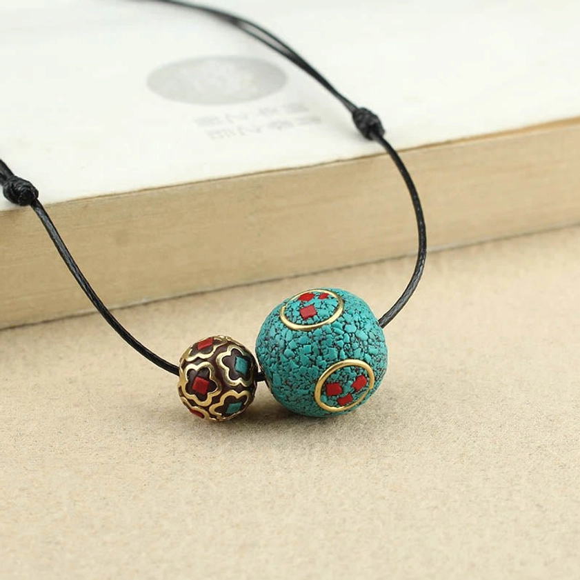 Turquoise and metal bead Buddhist necklace with adjustable black cord, close-up detail on book edge showing decorative beads