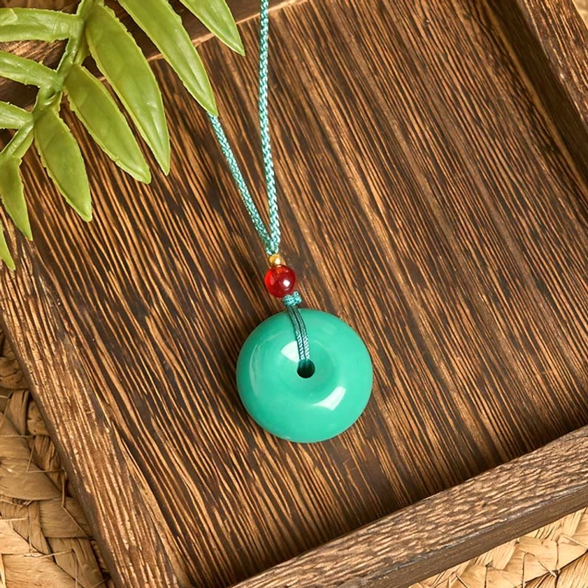 Natural turquoise peace buckle necklace on green rope - top angle view with foliage