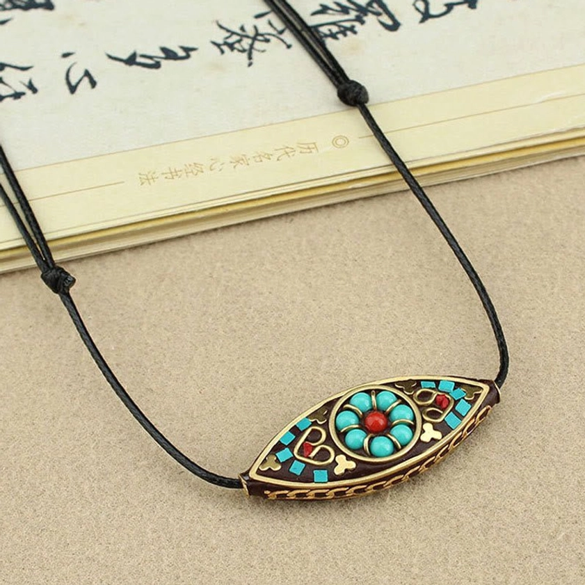 Dark brown turquoise Buddhist necklace pendant with floral ethnic pattern inlay near vintage book