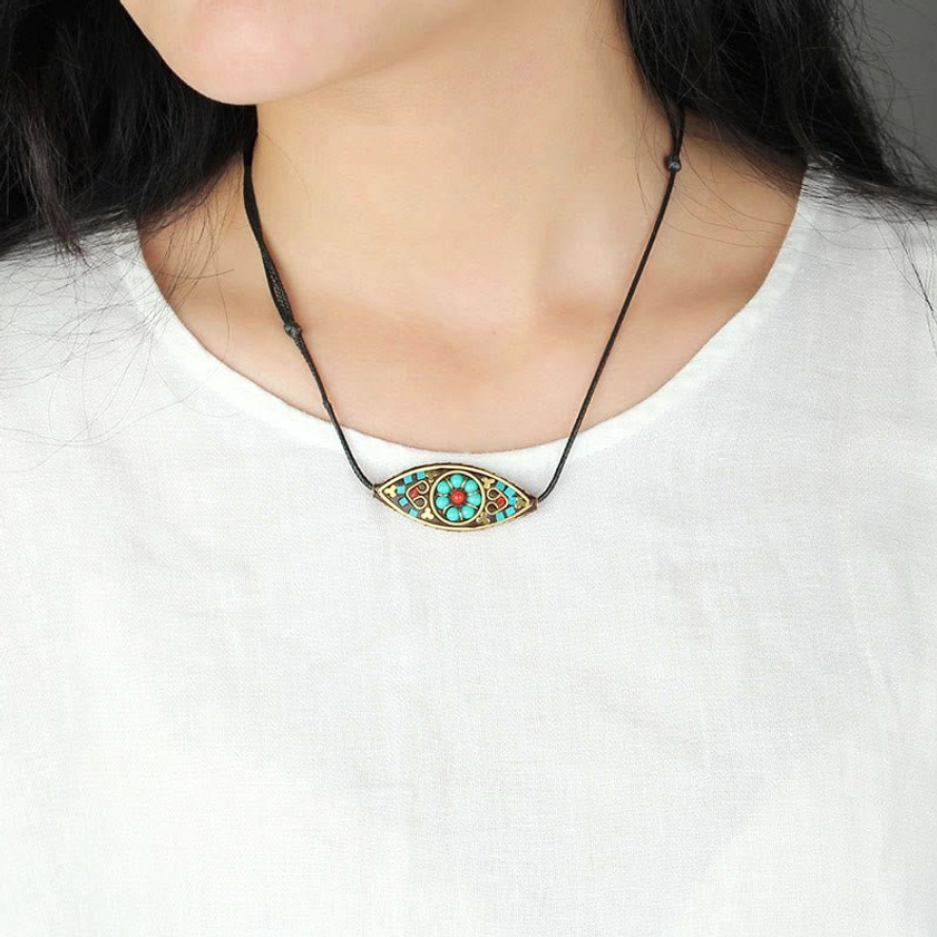 Turquoise Buddhist pendant necklace worn by woman in white top showing long cord styling at lower chest