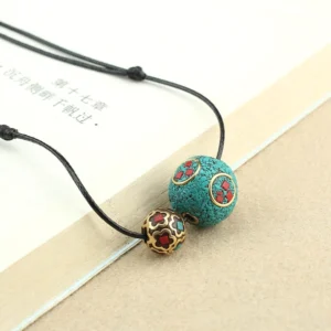 Turquoise double bead Buddhist necklace pendant with black wax cord displayed on beige desk with book, top view detail shot