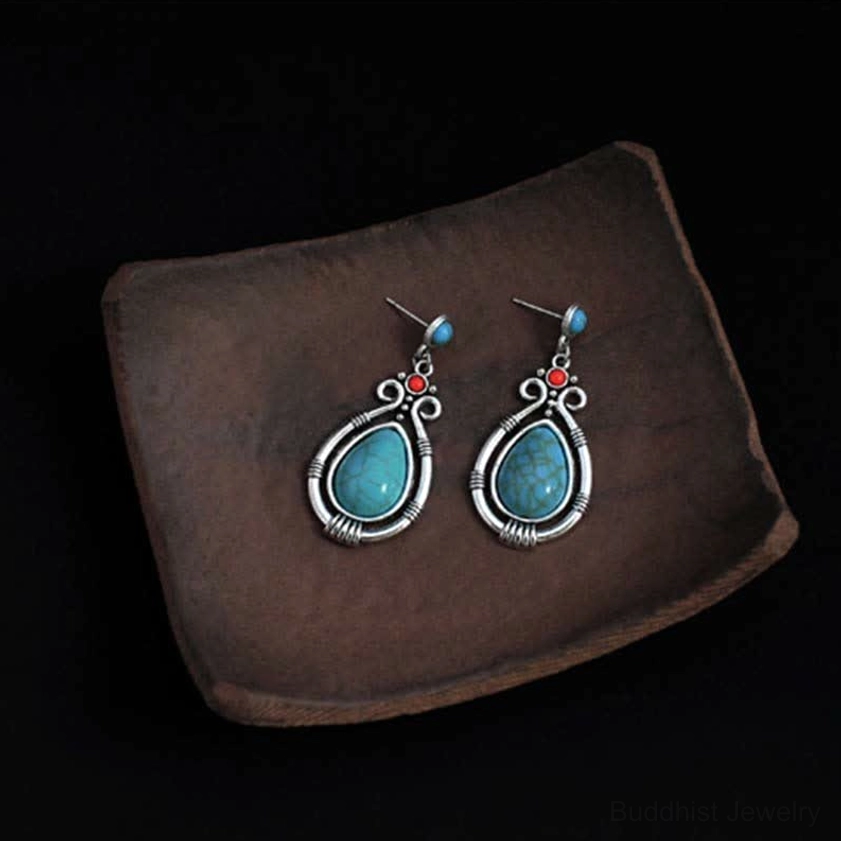 Pair of turquoise teardrop Buddhist dangle earrings neatly arranged on dark wooden surface