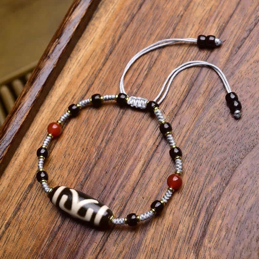 Turquoise and nine-eye dzi bead adjustable bracelet with brown woven rope, metal beads, and sliding knots on wooden desk
