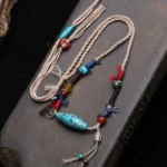 Turquoise dzi bead copper necklace pendant with braided cotton cord on dark wooden surface, showing complete Buddhist protection amulet design
