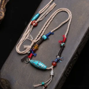 Turquoise dzi bead copper necklace pendant with braided cotton cord on dark wooden surface, showing complete Buddhist protection amulet design