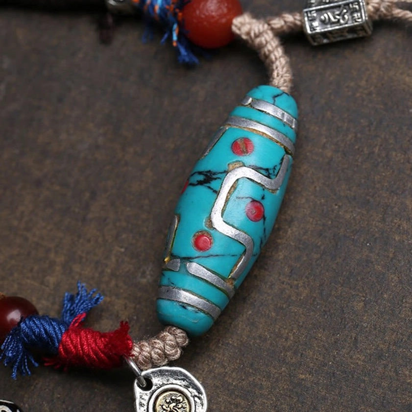 Main turquoise dzi bead pendant with silver inlay, red dot patterns, and silver brand charm on brown background