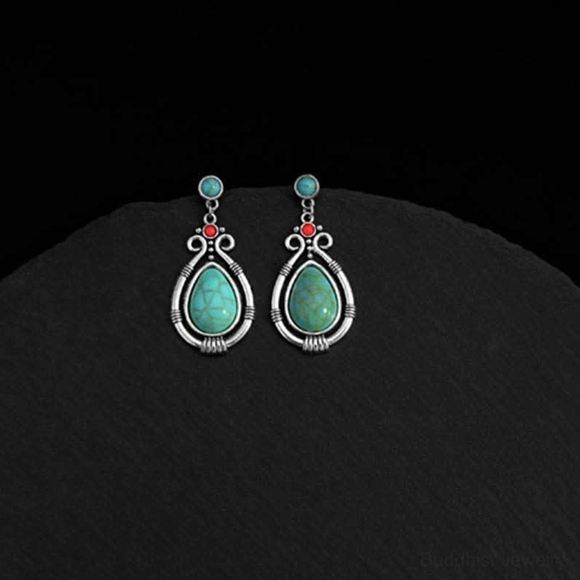 Turquoise teardrop dangle earrings arranged on black circular mat background