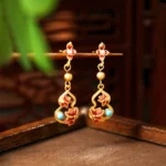 Turquoise cloisonné lotus drop earrings with copper alloy and genuine turquoise accents displayed on wooden tray with green foliage, front hanging view of Buddhist enlightenment earrings