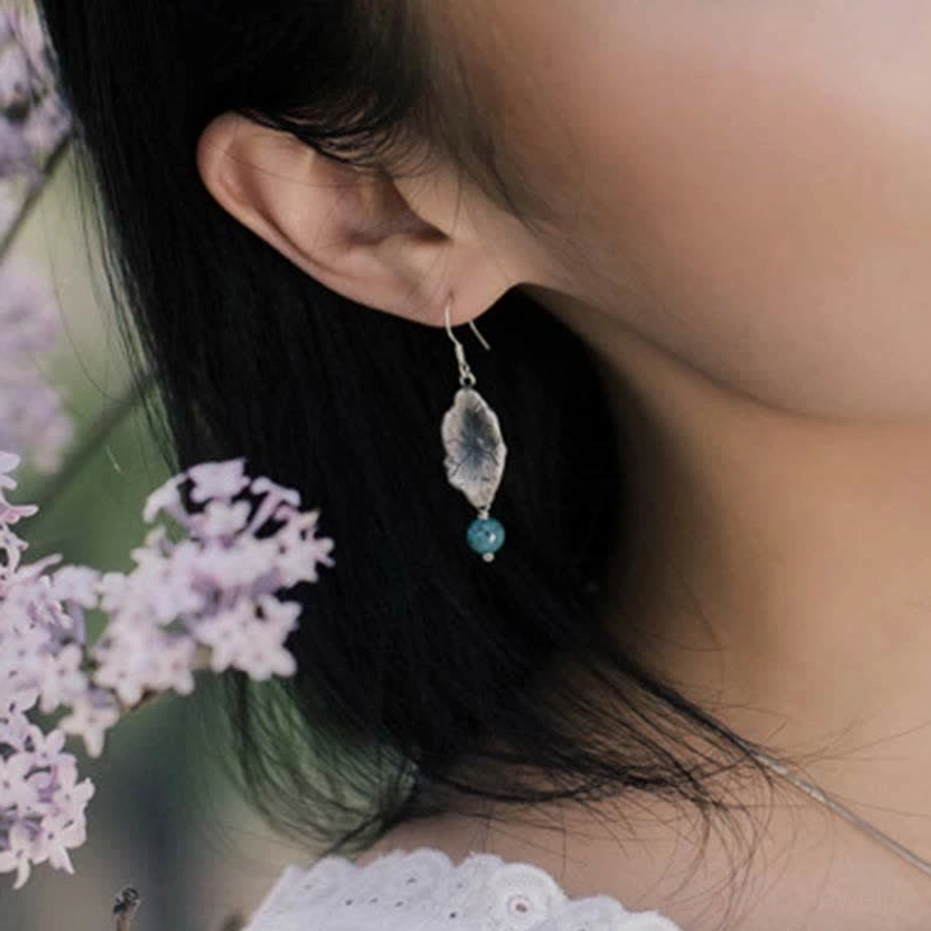 Woman wearing turquoise lotus leaf drop earrings outdoors with purple flowers