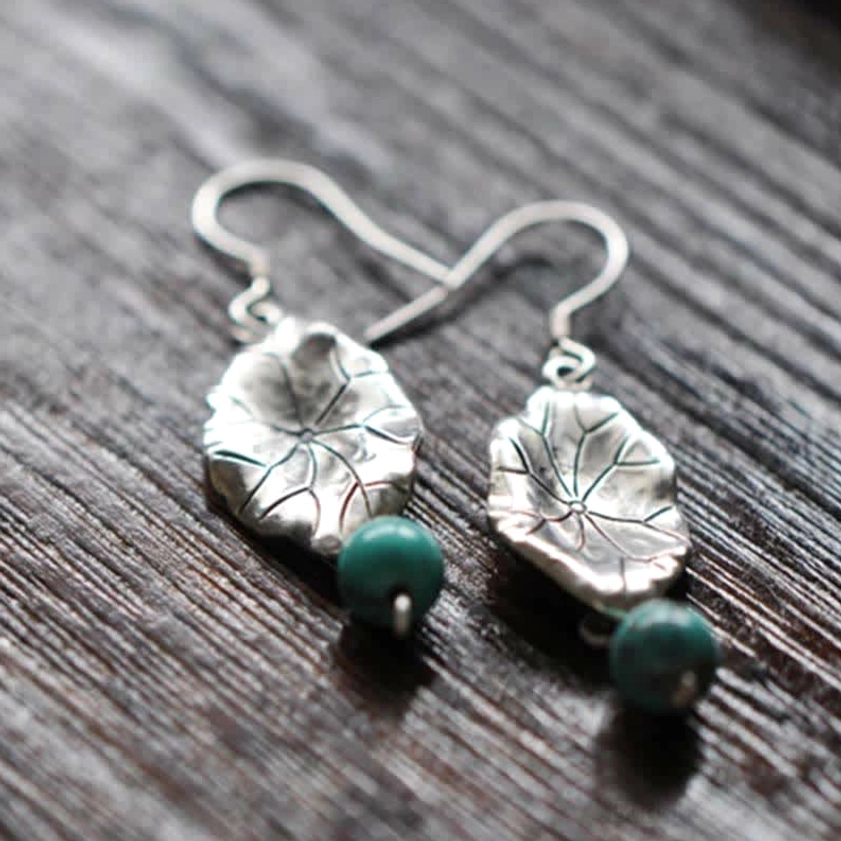 Round turquoise beads with embossed silver lotus leaf pattern drop earrings on wood