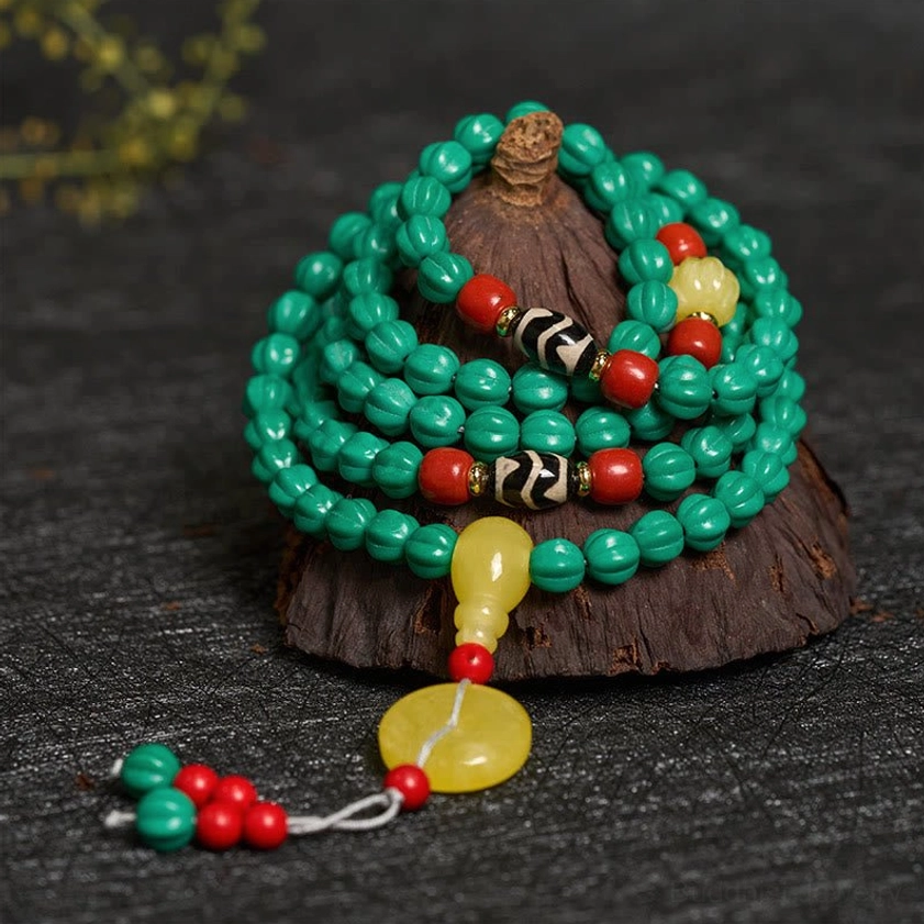 Coiled turquoise prayer mala from above showing bead texture, amber pendant and dzi beads on dark wooden base