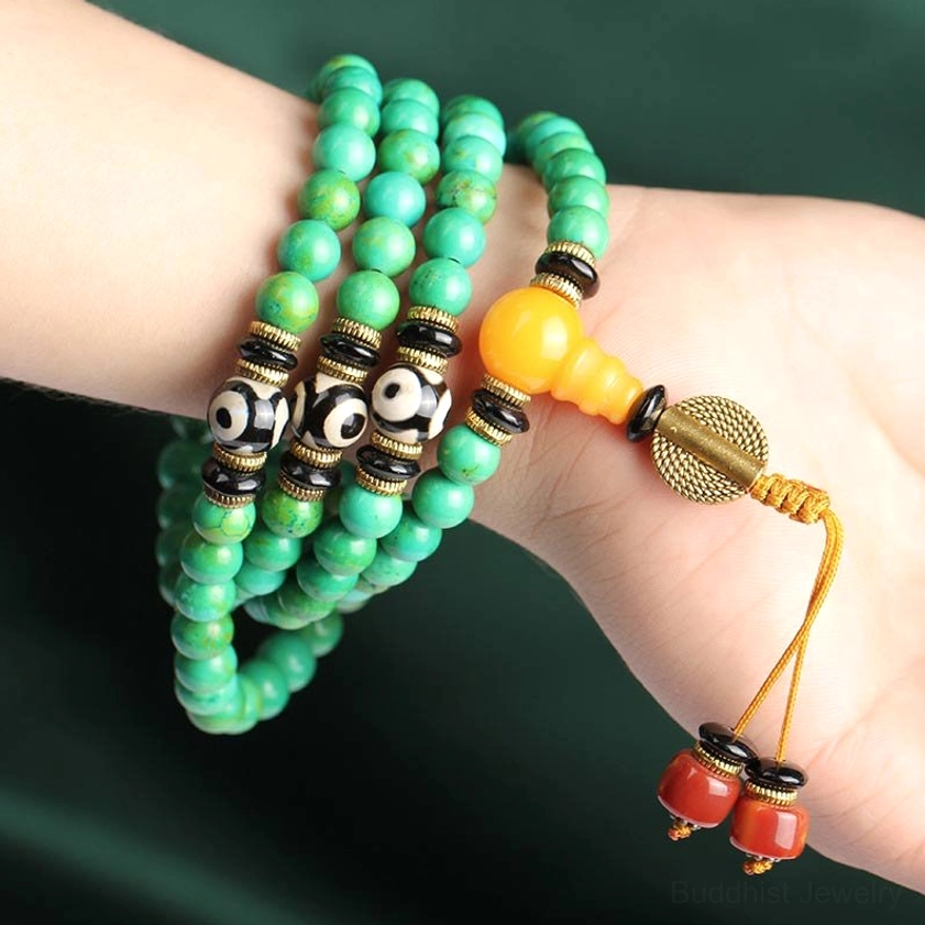 Turquoise mala bracelet worn on wrist showing beads, dzi accents, amber guru bead and red tassel in natural light