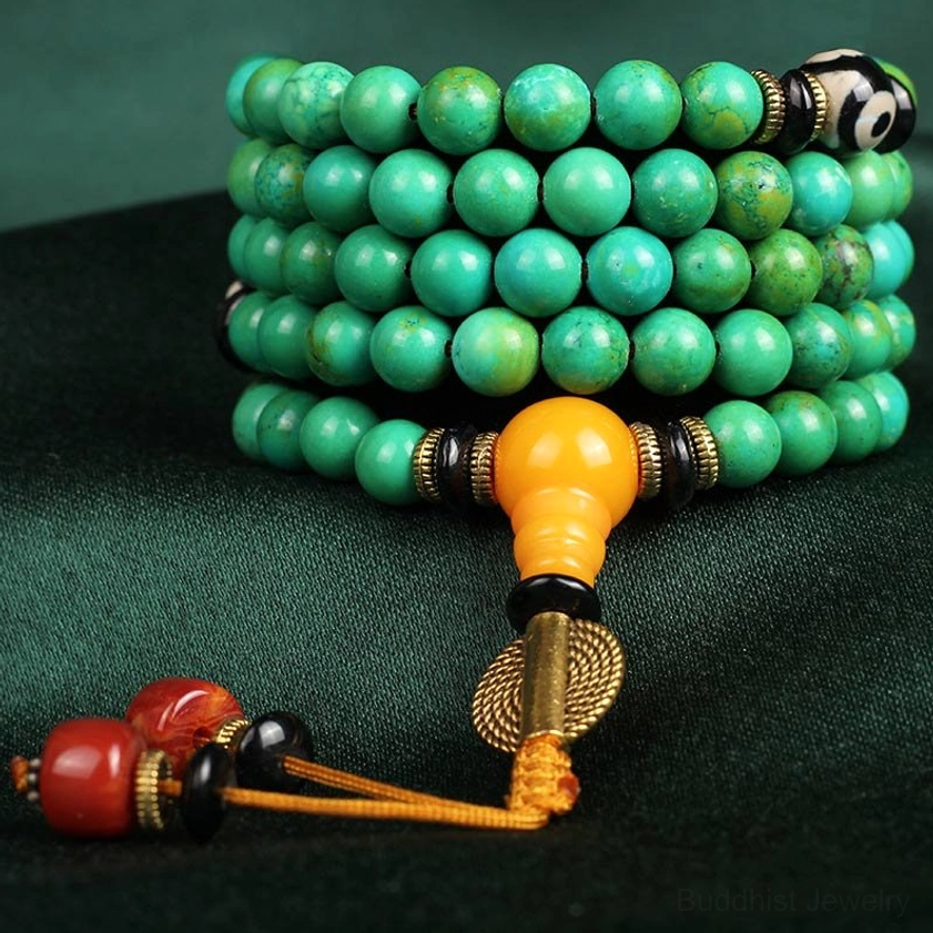 Coiled turquoise mala beads with golden metal spacers and amber guru bead on dark velvet background showing texture detail