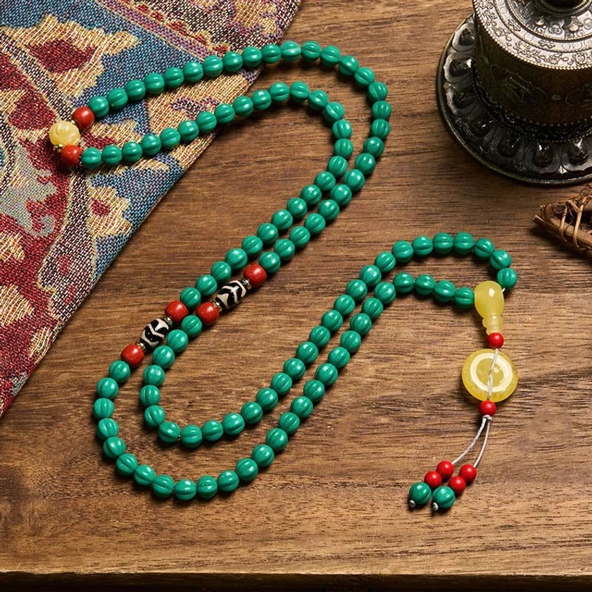 Flat-laid turquoise Buddhist mala necklace with extended tassel ornament on patterned fabric background