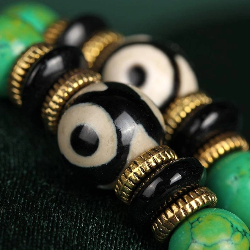 Macro close-up of turquoise mala beads showing three-eye dzi pattern, veined stone texture and golden metal spacer rings