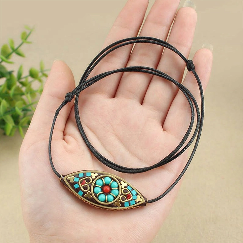 Close-up of turquoise marquise Buddhist pendant held in hand showing front design and twisted wax cord