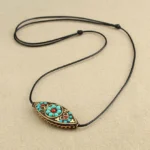 Turquoise marquise Buddhist necklace pendant with red beads on black wax rope, flat lay view on light background