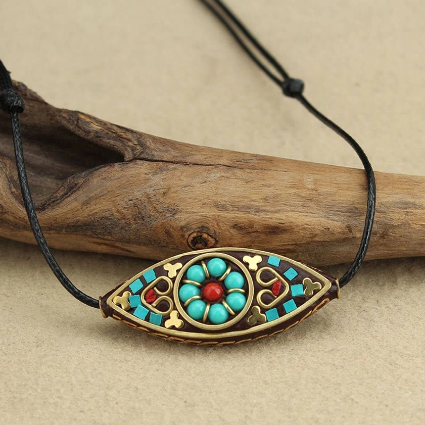 Turquoise eye-shaped marquise pendant with colorful stone inlays on Buddhist necklace with driftwood background