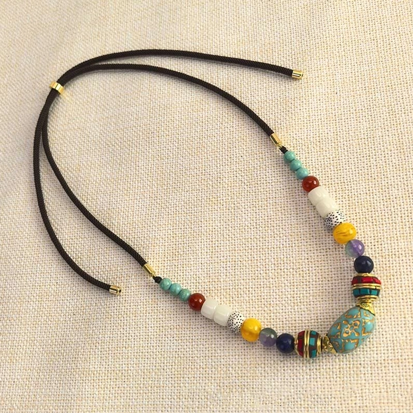 Side view of adjustable turquoise Buddhist necklace cord with beads on linen background
