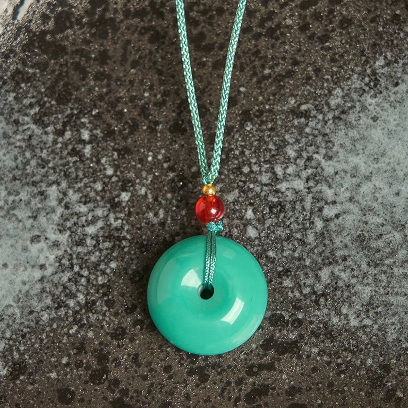 Turquoise stone peace buckle pendant with red and gold beads - flat lay on textured surface