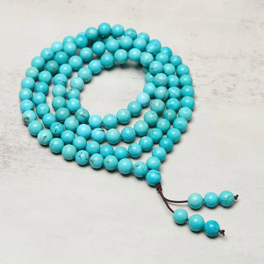 Full-length turquoise 108-bead mala necklace spread out with tassel pendant on neutral background