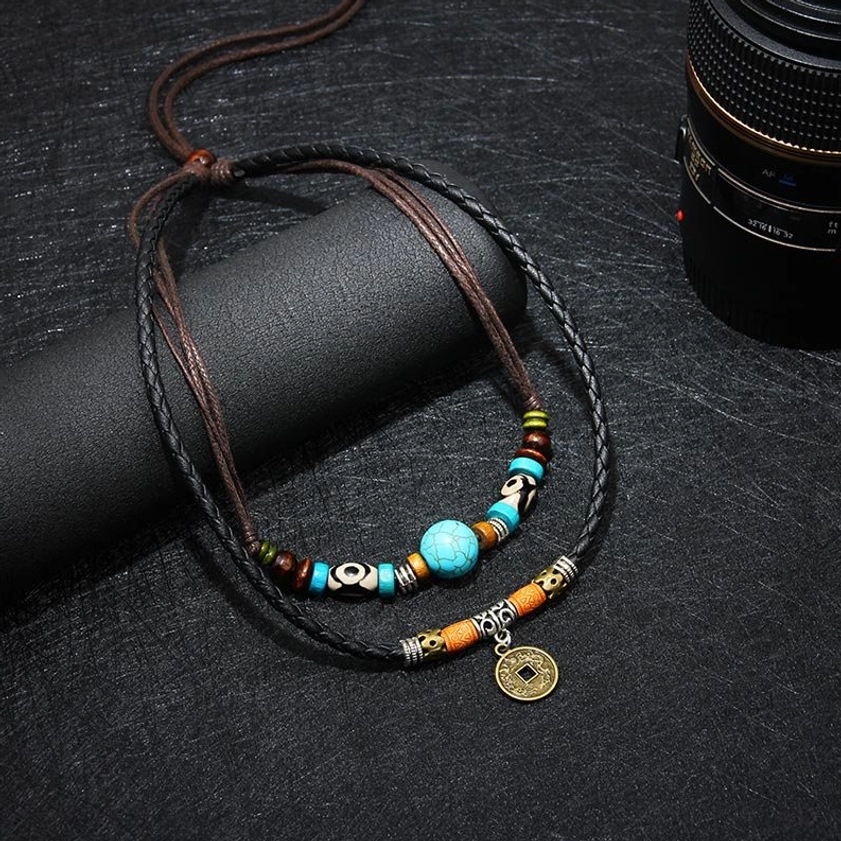 Layered turquoise Buddhist necklace with dual-tone braided straps and vintage ethnic coin charm, angled studio photography