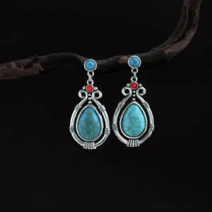 Vintage turquoise teardrop Buddhist dangle earrings with silver filigree frame on dark background with natural elements