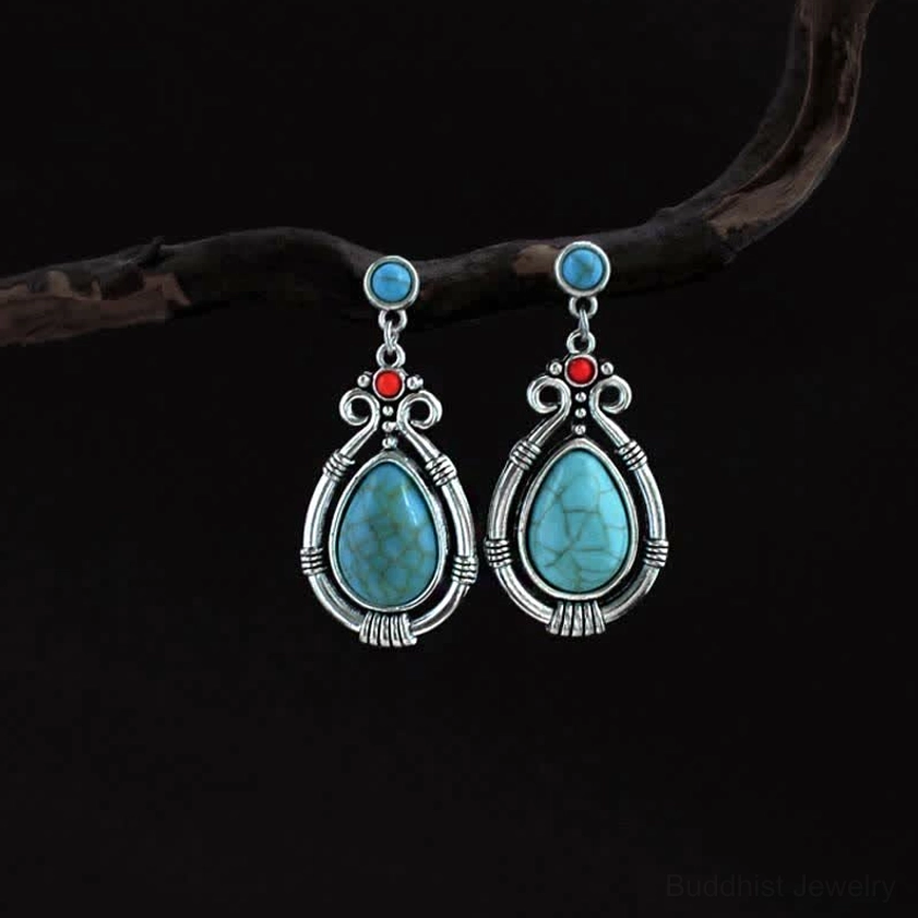 Vintage turquoise teardrop Buddhist dangle earrings with silver filigree frame on dark background with natural elements