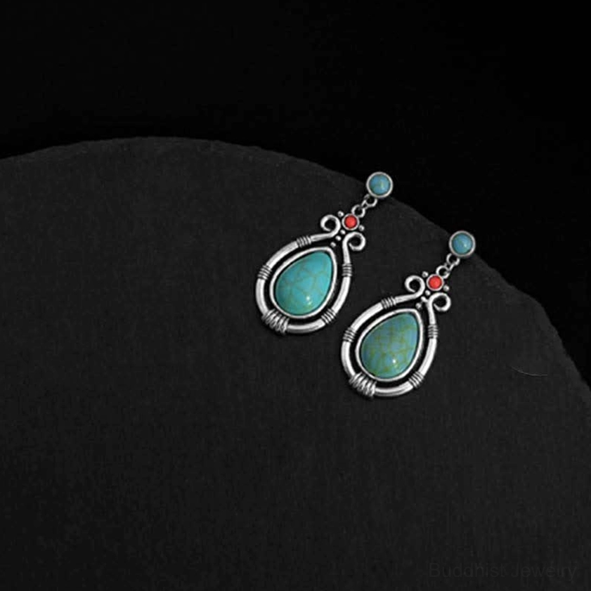 Two turquoise Buddhist dangle earrings placed separately on dark matte background showing individual design