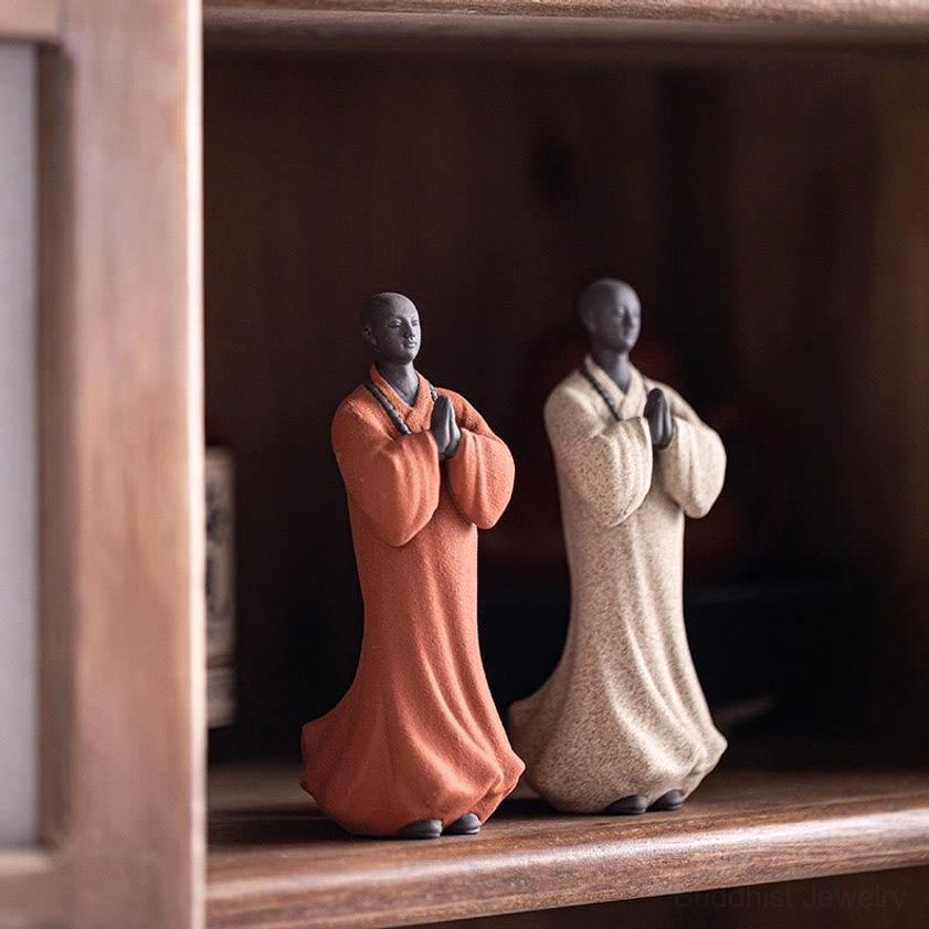 Two handcrafted ceramic monk figurines in terracotta and white displayed together in wooden cabinet interior