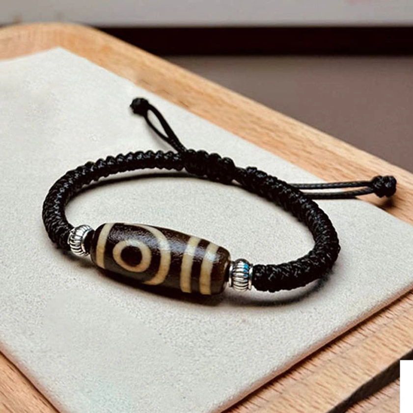 Two-eye dzi bead bracelet flat lay view showing dual-eye pattern with black braided cord and silver spacers