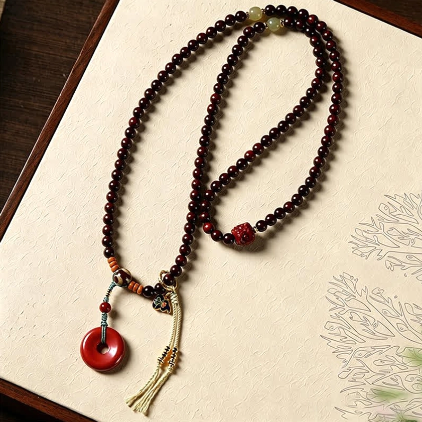 Unstrung 108 bead mala showing individual red rosewood beads with small red accent bead and peace buckle pendant on vintage patterned paper