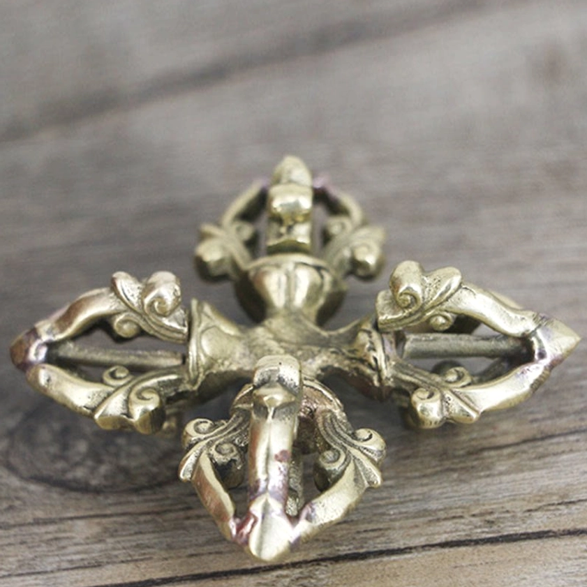 Overhead bottom view of copper vajra showing brass tone centered floral core and carved scroll prongs
