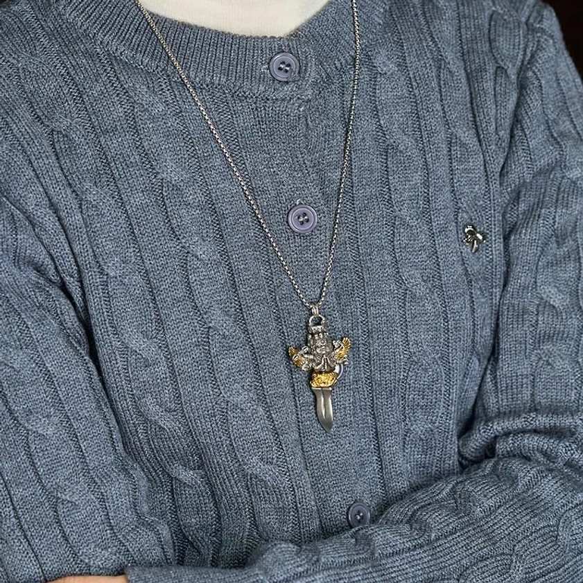 Person wearing six-armed vajra copper necklace as daily spiritual jewelry, chest-level view on gray knitted sweater showing silver gold and dark metal tones